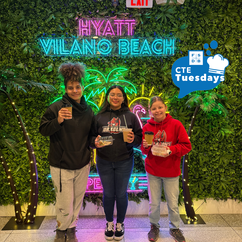 Three students holding coffee and treats smile by a grass wall with led lights that say "Hyatt Vilano Beach"