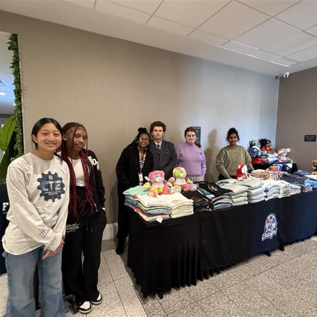 Group of students smile with the DB Designs merch inside the hotel building. 
