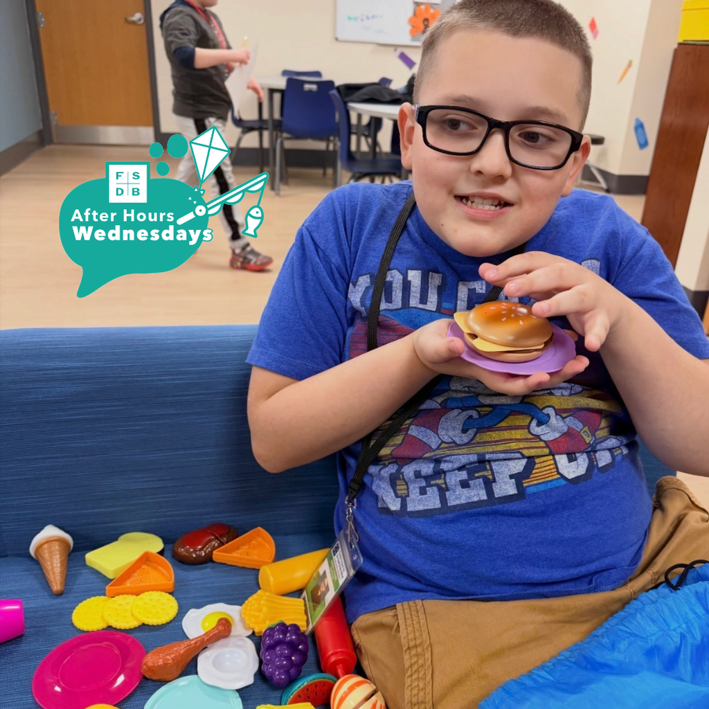 A student is holding play toy food smiling for his photo. 