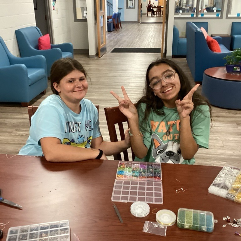Two middle school girls smile while working on crafts at a table inside the dorm.