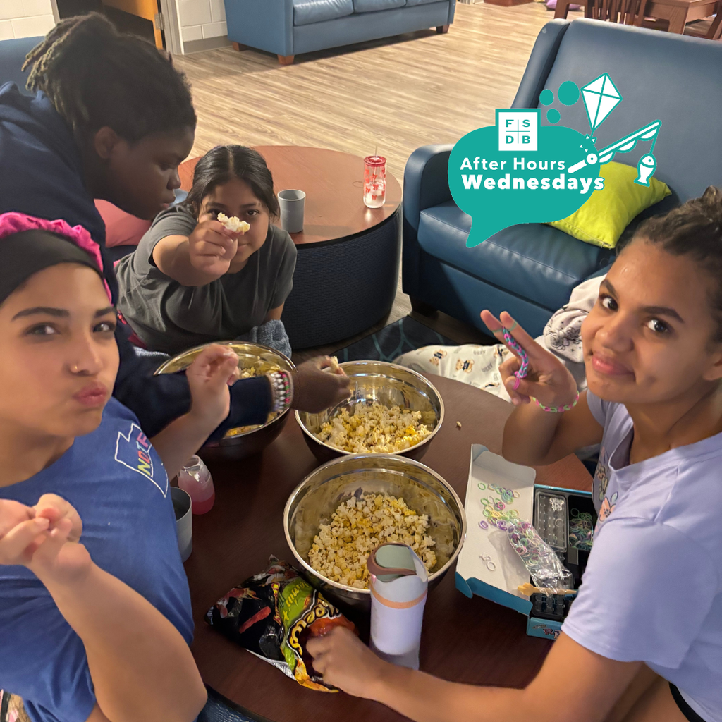 A photo of middle school girls smiling with their popcorn at a table inside the dorms.