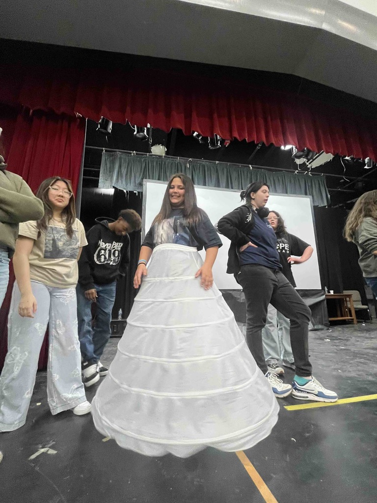 A student wearing a long white skirt smile on stage. 