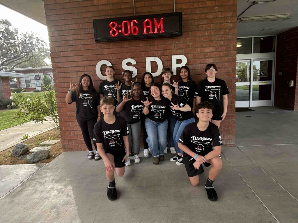 Group of middle school students and staff sign "ILY" and smile for the photo with the CSDR sign in the background. 