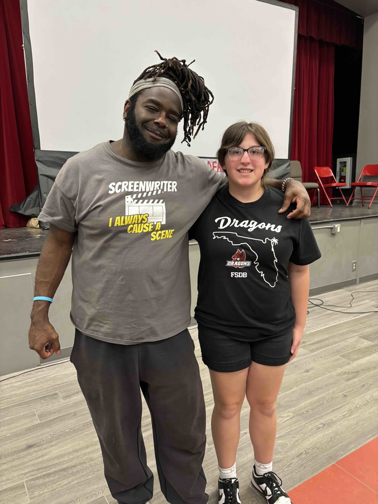 A student smiles with a person who is wearing a shirt that says "screenwriter, I always cause a scene" inside the CSDR building. 