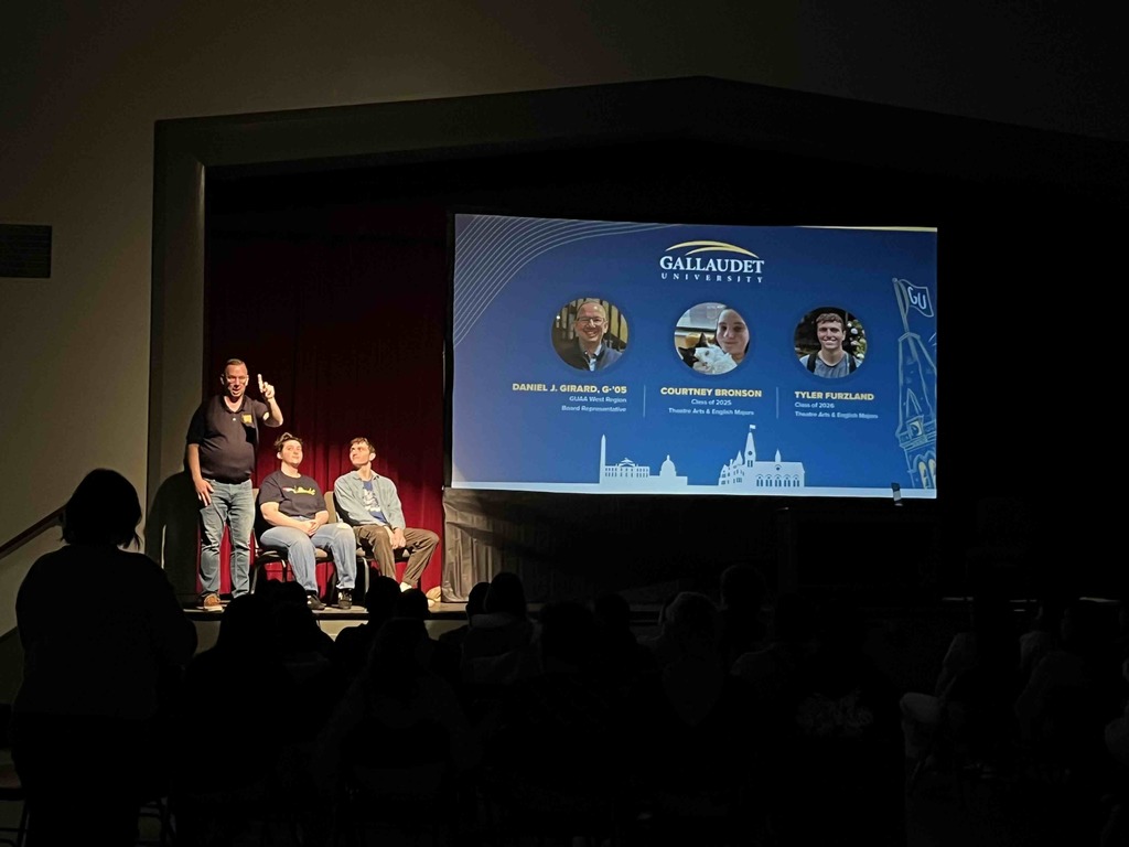 Three guest speakers on stage speaking to the audience. 