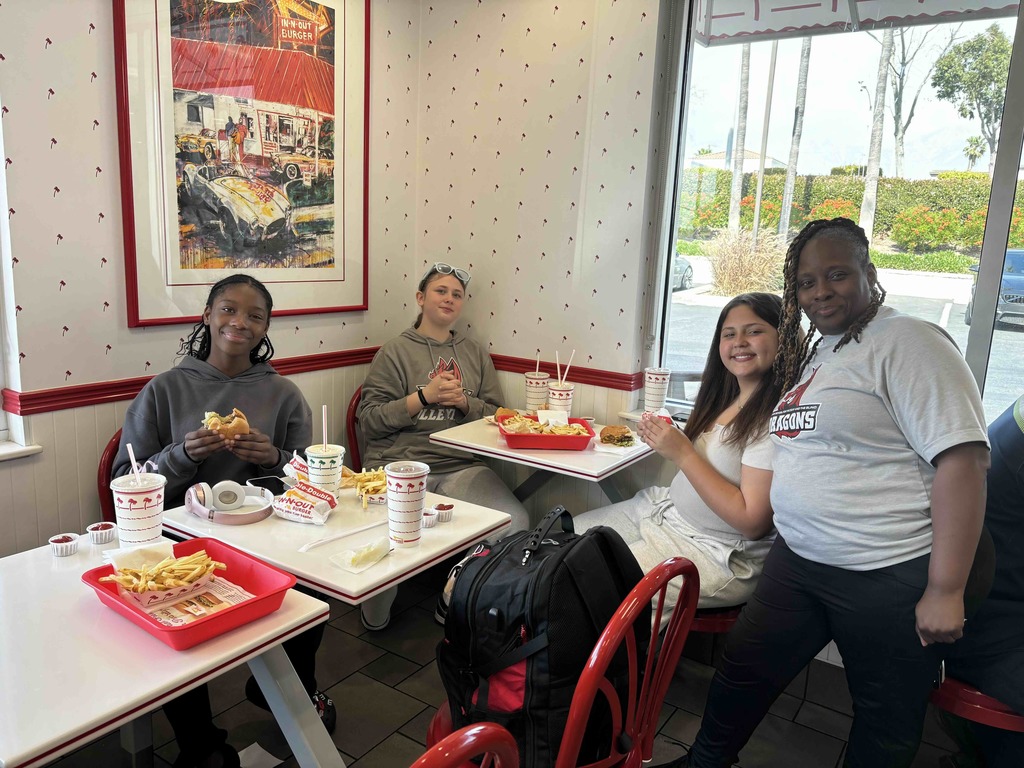 Staff member and three students smile and eat inside In-and-Out burger place. 