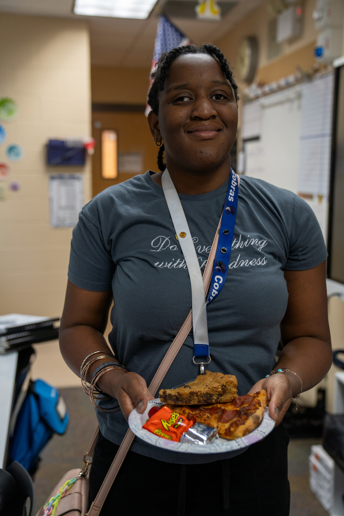 A student smiles with her pizza, brownies and candy inside the classroom. 