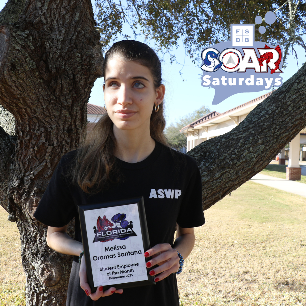 Melissa is wearing a black shirt that says "ASWP" with her hair up and some on her shoulder. She is holding up an award that says "Melissa Oramas Santana Student Employee of the Month December 2025"