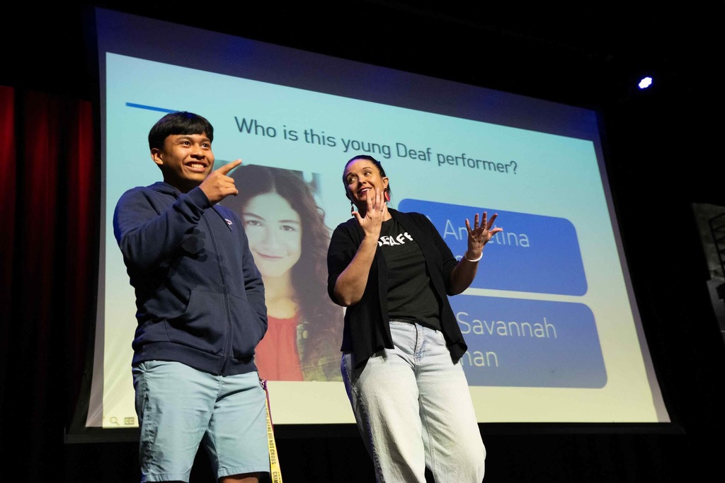 Dr. Renca and a student stand on stage talking to the crowd the A or B question on the screen inside Kirk.