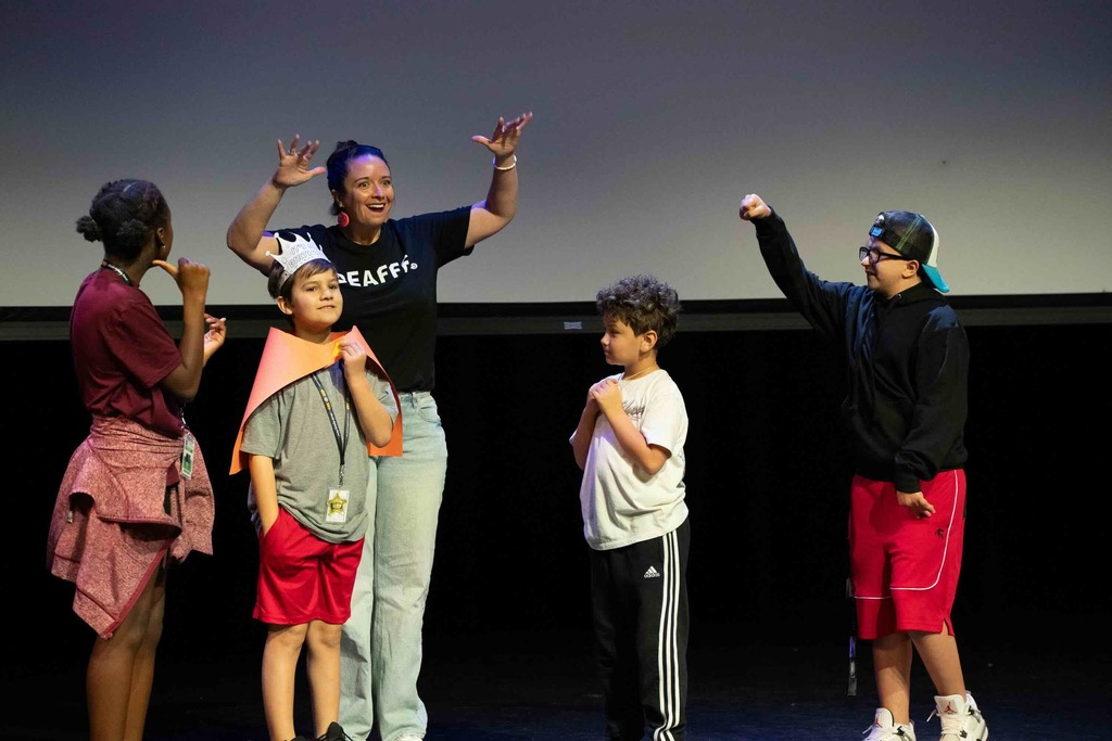 A group of elementary deaf students stand on stage with Dr. Renca inside Kirk.