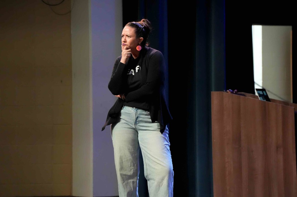 Dr. Renca Dunn hold her hands by her chin and questioning the crowd on stage in Kirk.