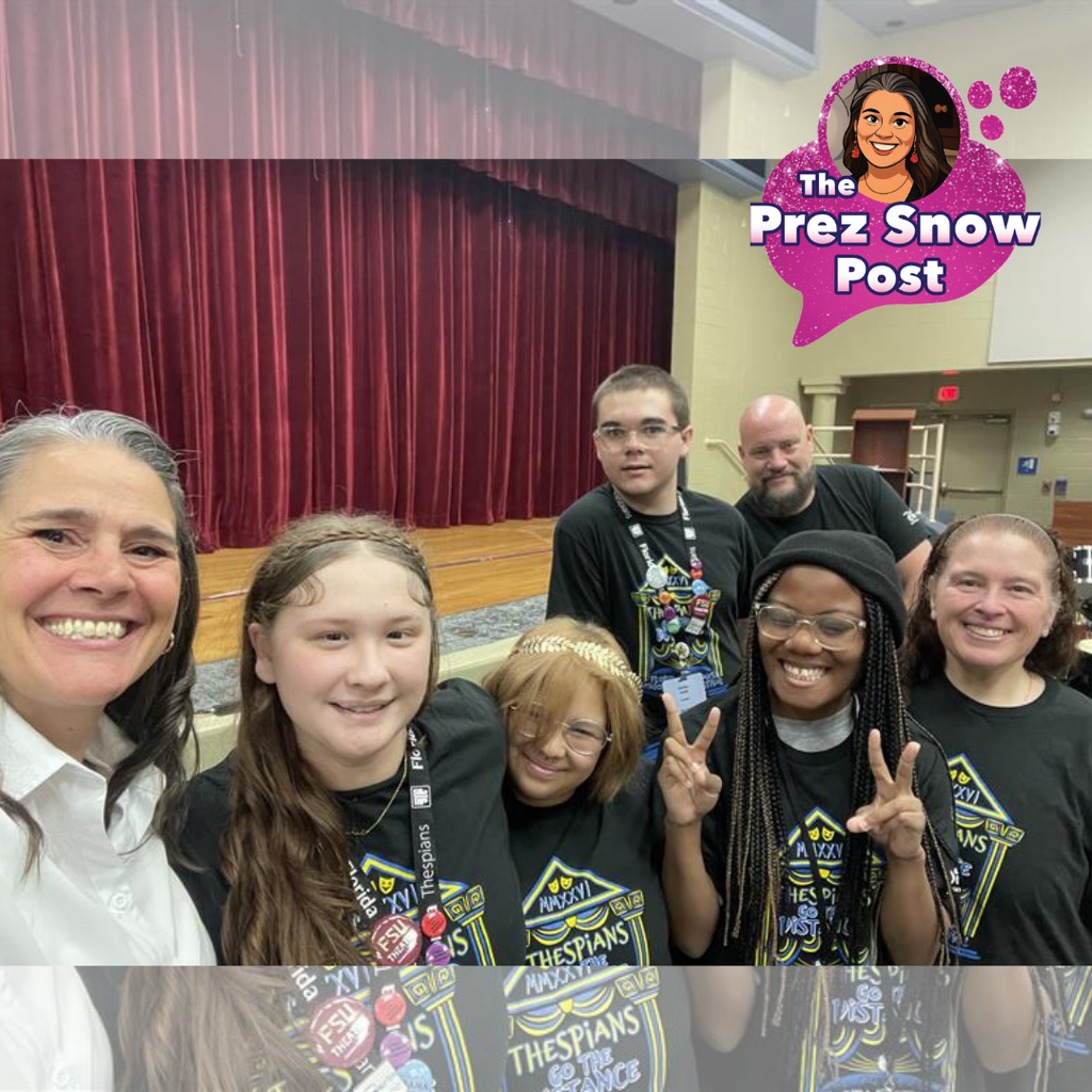 President Snow is taking a selfie with members of FSDB Blind High School’s Thespian Troupe inside a school auditorium. The group (four students and two sponsors) stands together near the front of a stage with tall maroon curtains in the background, wearing matching black Thespian T shirts and lanyards. A few students are positioned close to the camera, with one student holding up peace signs.
