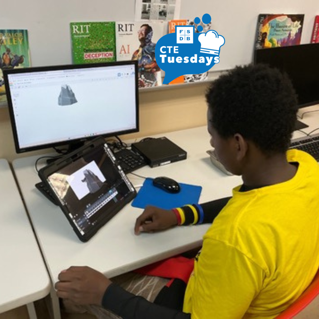 A student wearing a yellow shirt working on his project with the tablet and computer inside a classroom.