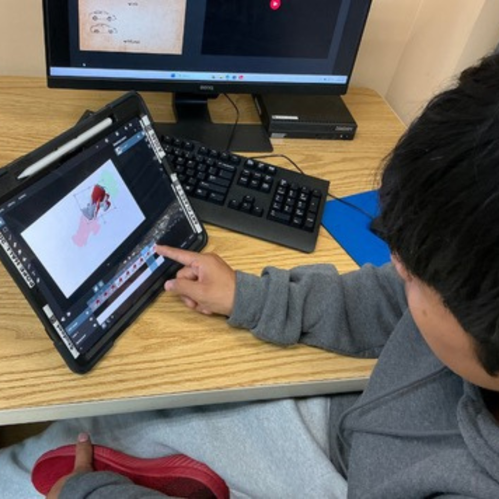 A student working on his project on the tablet and computer inside the classroom.