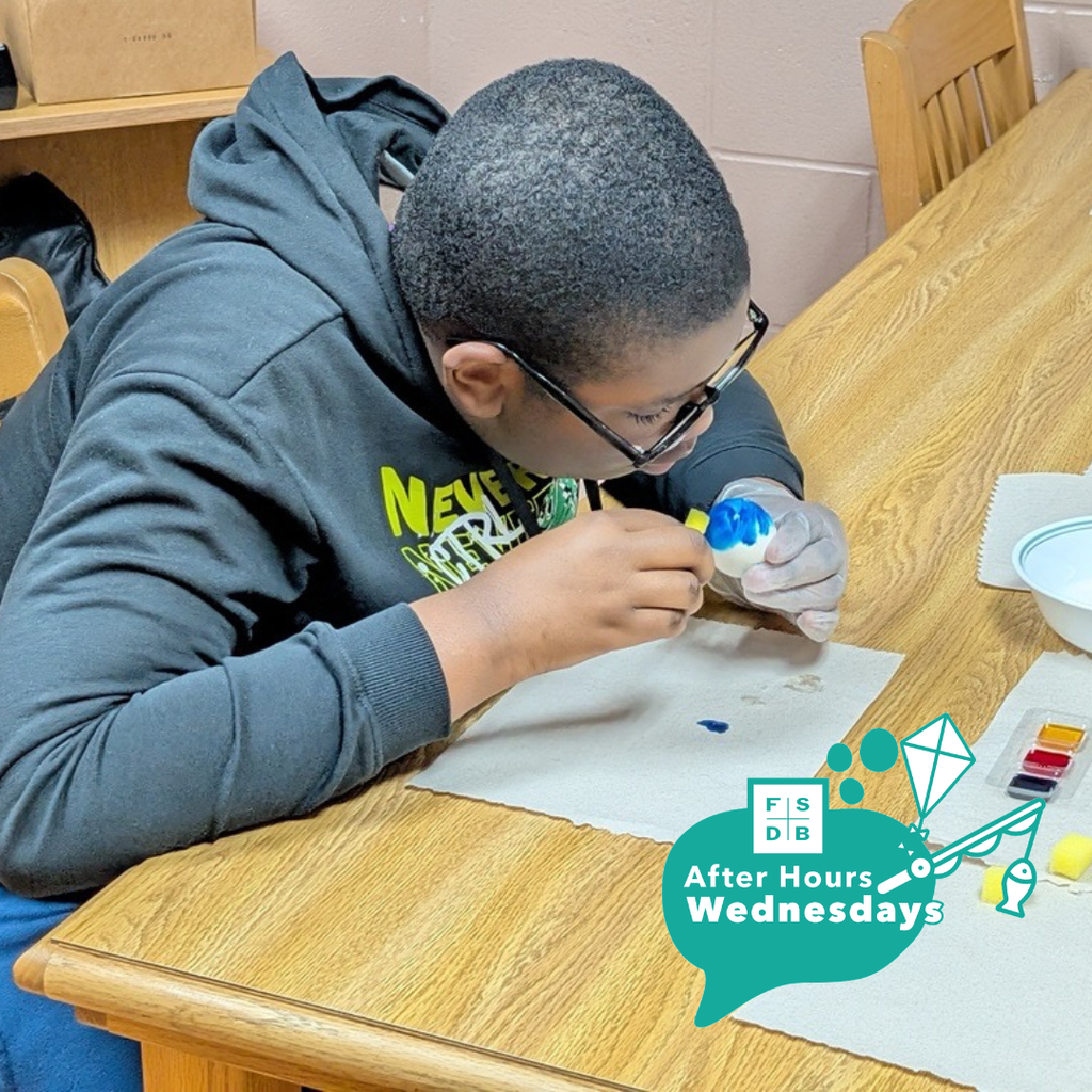 A student is sitting at a table and painting the egg blue.