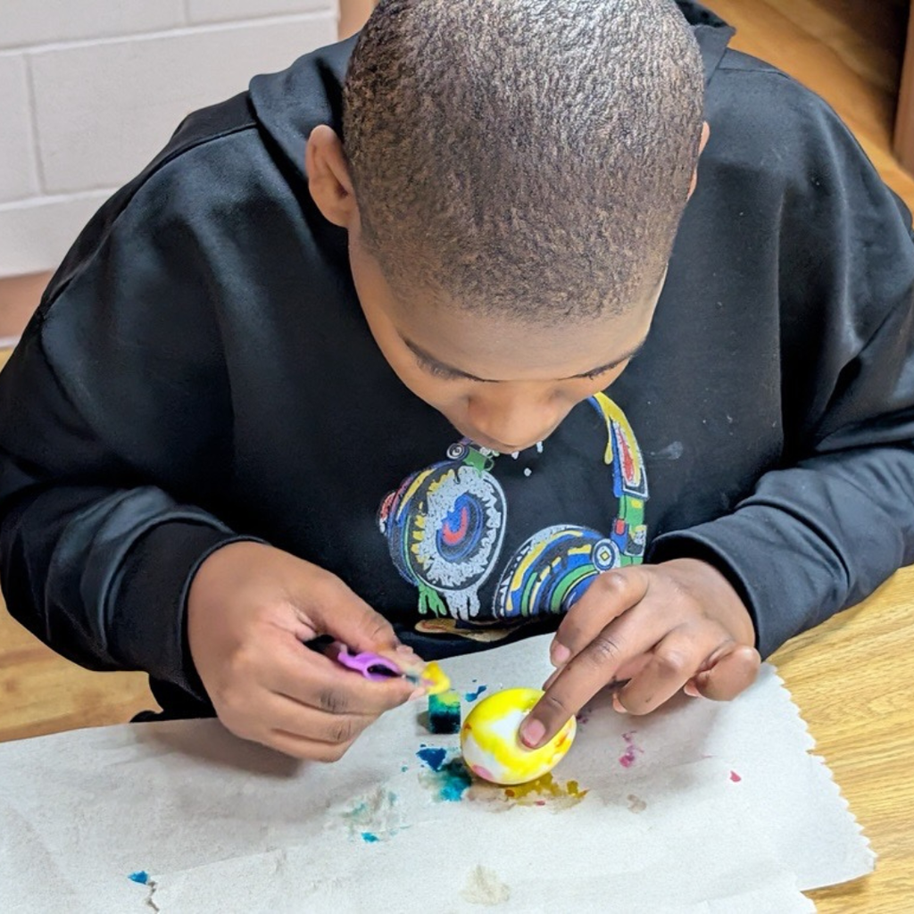A student is sitting at a table and painting his egg yellow.