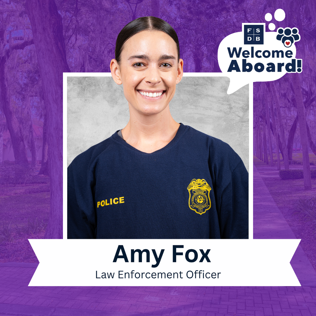 Amy is wearing a navy blue shirt with the police logo on the corners of her chest smiles for a photo with a silver backdrop and purple background. Below the photo is a white textbox that says "Amy Fox, Law Enforcement Officer"