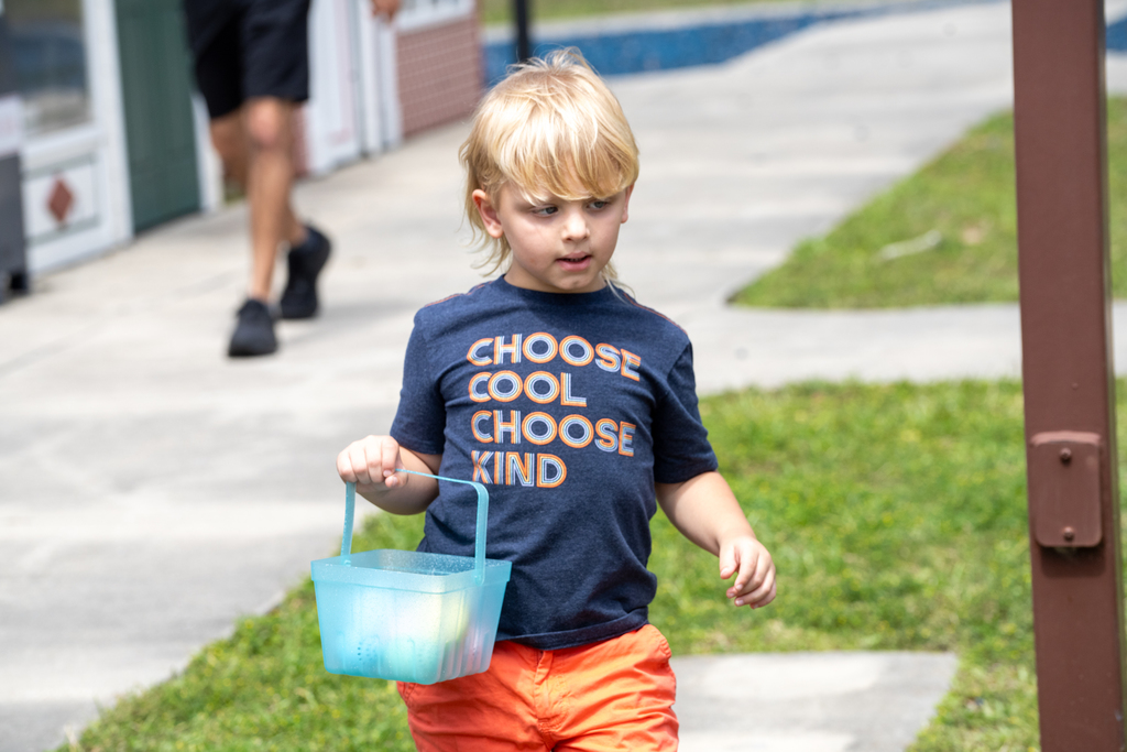 A student holds his blue easter basket with eggs inside walking through Kids Town.