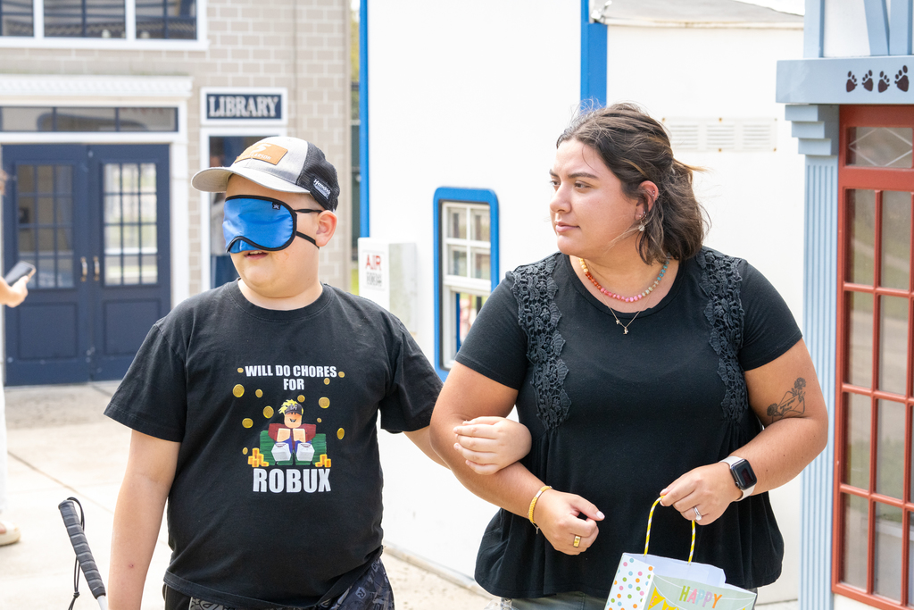 A staff member help guide a student who is wearing eye mask to look for easter eggs outside of Kids Town.