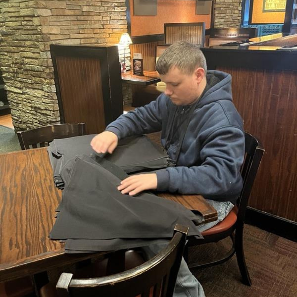 Allan is folding napkins at a table inside a restaurant.