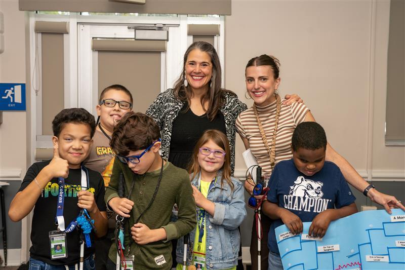 Group of blind students smile with President Snow and their teacher in the blind department inside CLD.