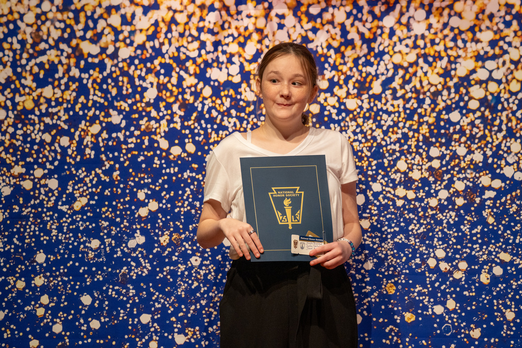 Kayla is holding her NHS booklet and smile for the photo with a blue and sparkle background.