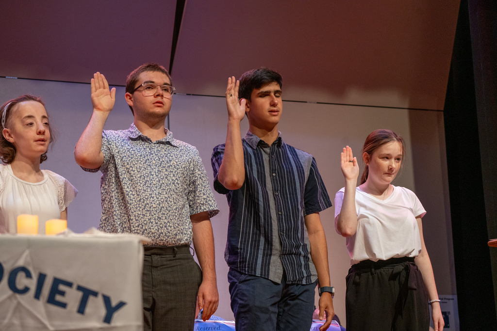 Inductees hold their hand up on stage in the music building.