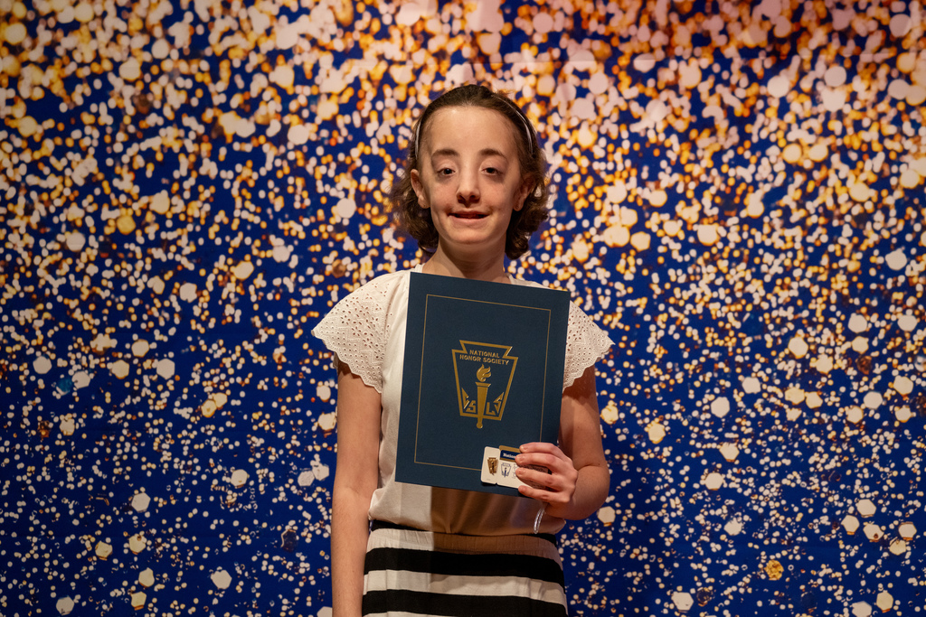 Danika holds her NHS booklet and smiles for a photo on stage with a blue and gold sparkle backdrop.