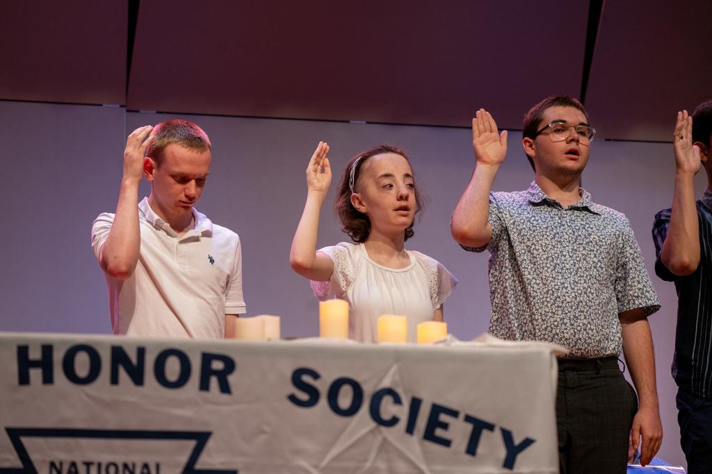 Inductees hold their hand up on stage in the music building.