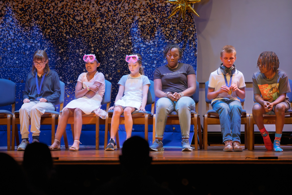 A group of students sit in chairs on stage in the Music Building.