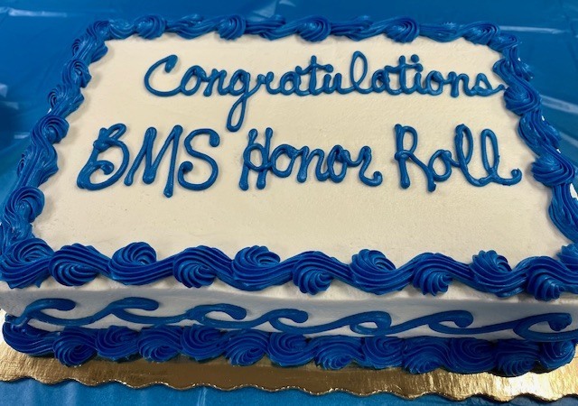 A closeup of the cake that is covered in white and blue text that says "Congratulations BMS Honor Roll;"