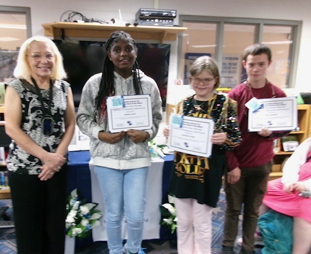 Students smile holding their certification with the Blind principal inside the library. 