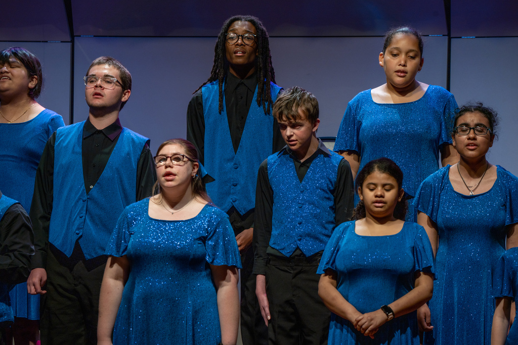 A group of FSDB students wearing blue concert outfits singing on stage in the Music Building. 