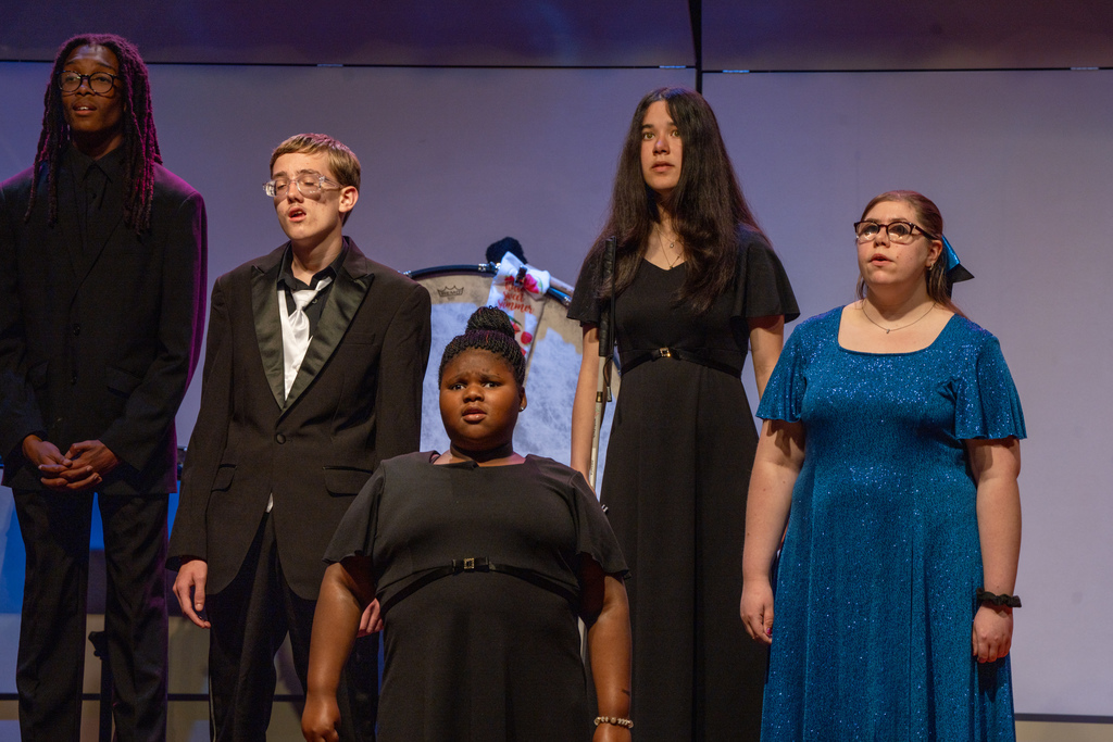 A group of FSDB students wearing blue and red concert outfits singing on stage in the Music Building. 