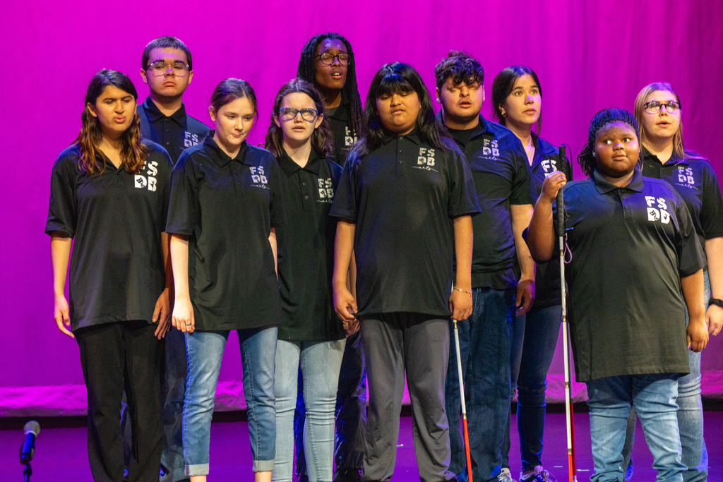 Group of BHS Chorus wear matching black shirt collars standing on stage in Kirk singing to the audience. 