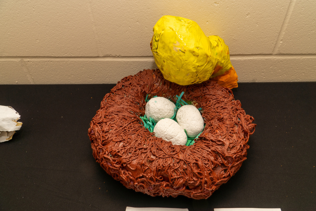 A creation made by a blind student of a yellow chicken looking down on its brown nest with three white eggs ready to hatch. 