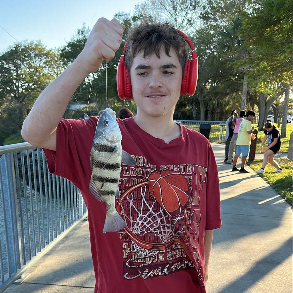 A boy wearing red headphones hold the fish he caught outside by the water at FSDB.