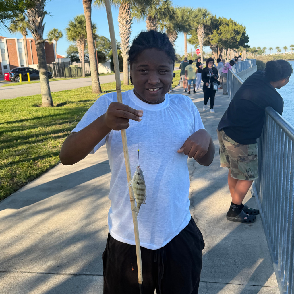A boy hold his fishing rod with fish hooked on it outside by the water at FSDB. 