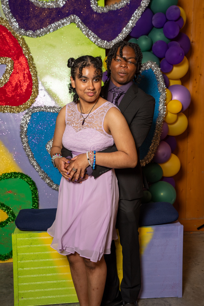 A couple smiles for a photo with the Mardi Gras backdrop inside the barn. 