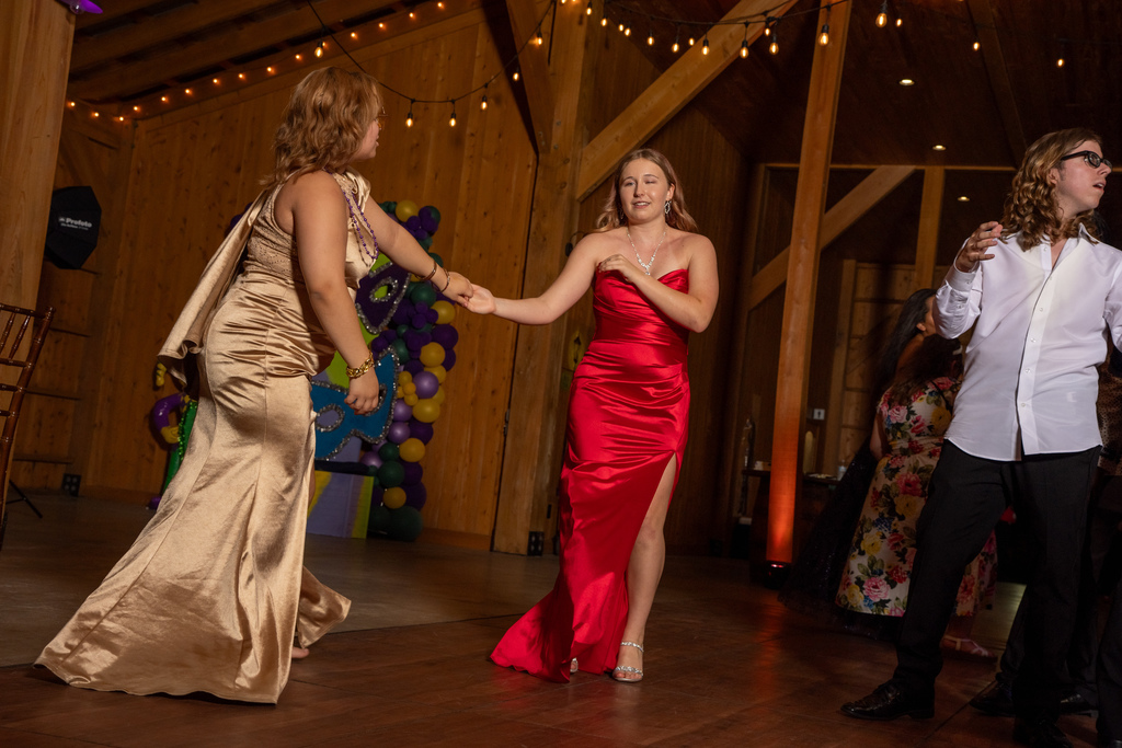 Two students dressed in gold and red hold hands and dance on the dance floor of the barn. 