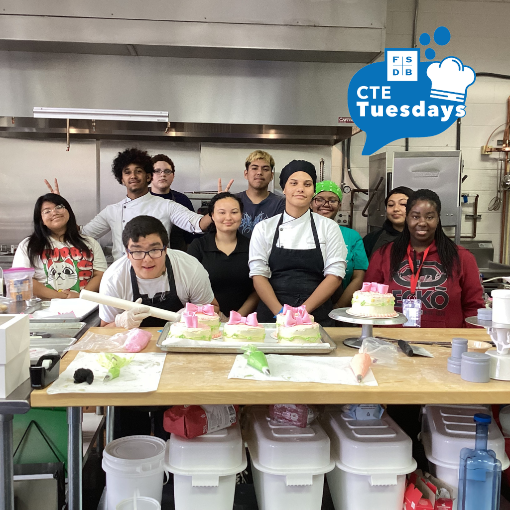 Group photo of the Culinary Arts students smile for a photo with the Mother Day cake inside the kitchen. 