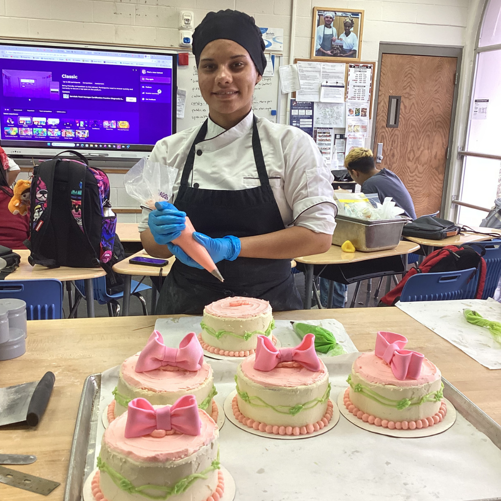 A student smiles as she puts icing on the cakes inside the kitchen. 