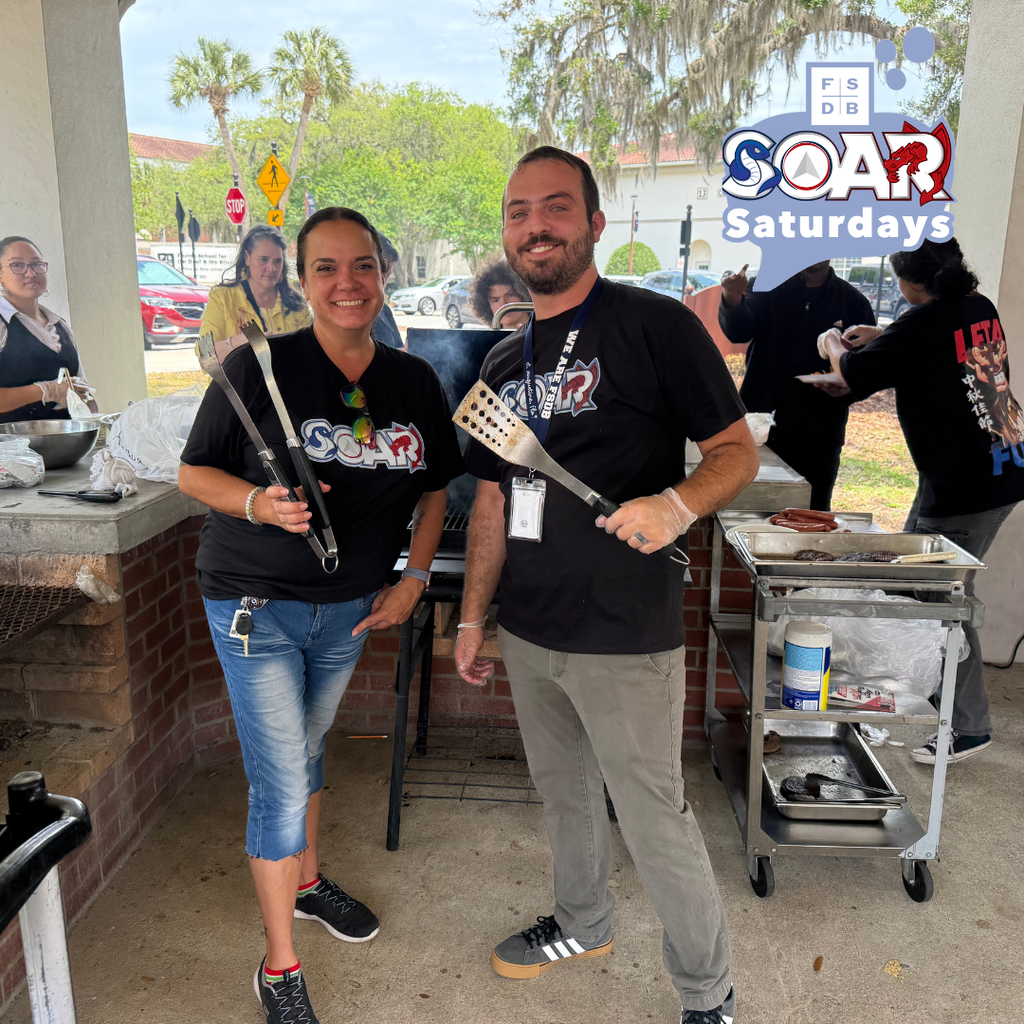 SOAR Sponsors wearing matching SOAR shirts holding grill essentials smiling for a photo by the grill outside.