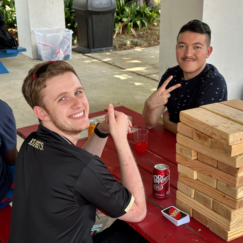 Two students sit and play large Jenga smile for a photo outside the pavilion.