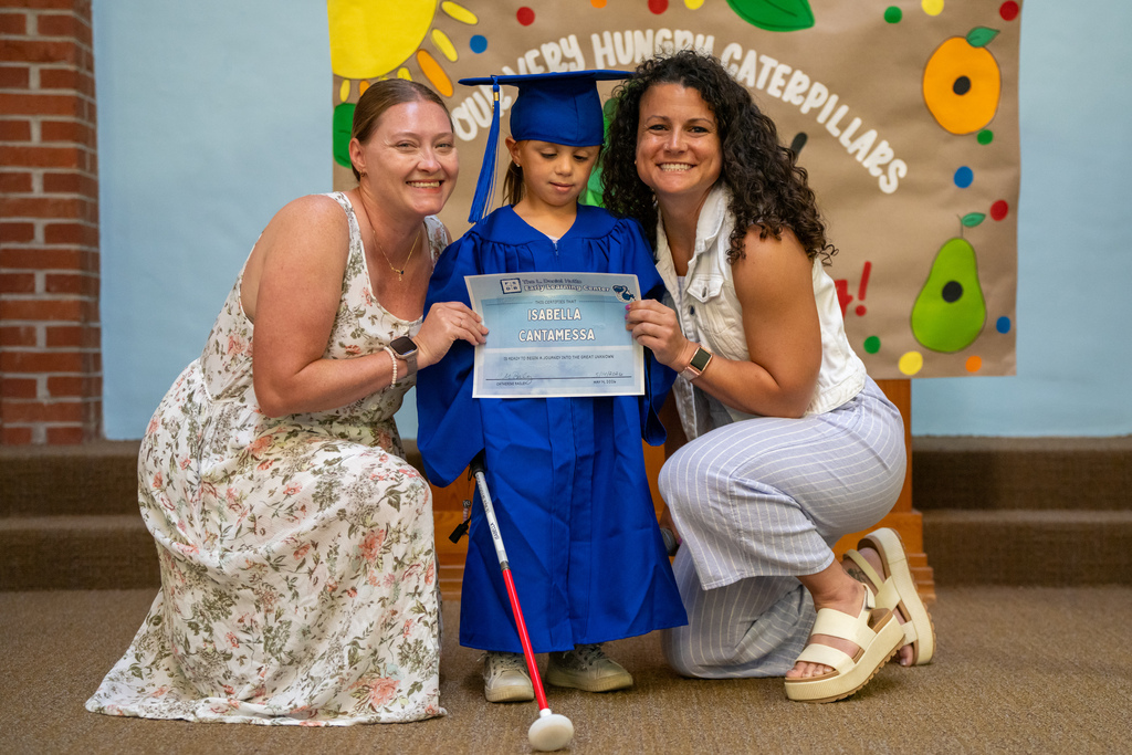 ELC Blind Graduate wearing blue cap and gown smile for a photo with two ELC staff inside the Chapel.