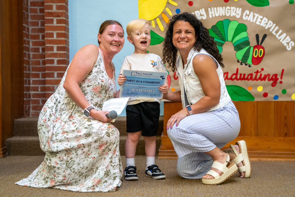 ELC Teacher and ELC Director smiles with a ELC student holding his certification on stage in the Chapel. 