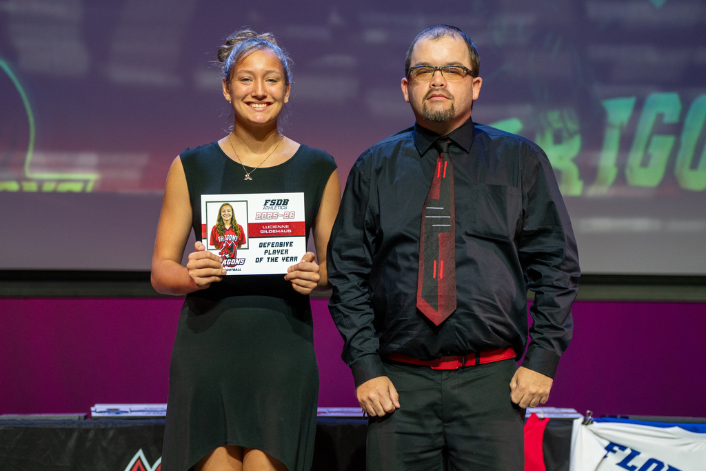 A staff member smile with a student who won an award on stage in Kirk.