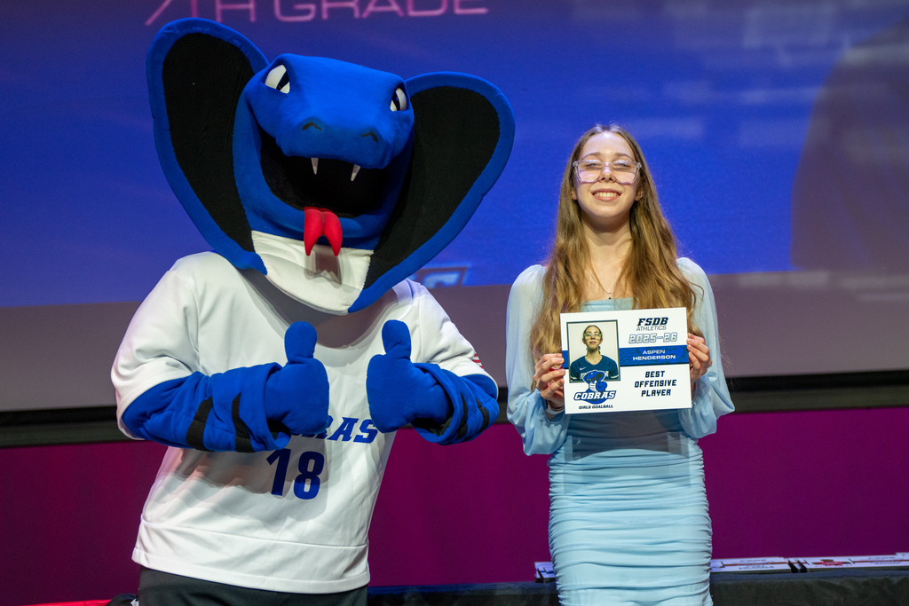A student who won an award smile on stage with the Cobra mascot.