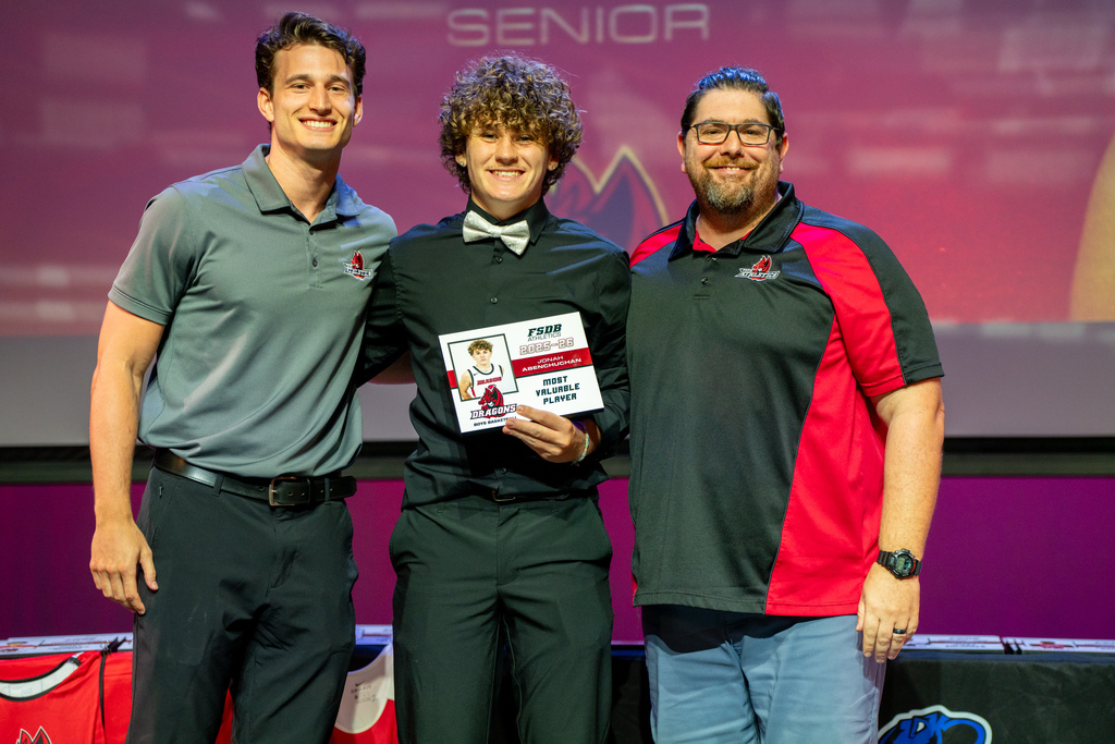 Two Basketball coaches smile with a player who won an award on stage in Kirk.