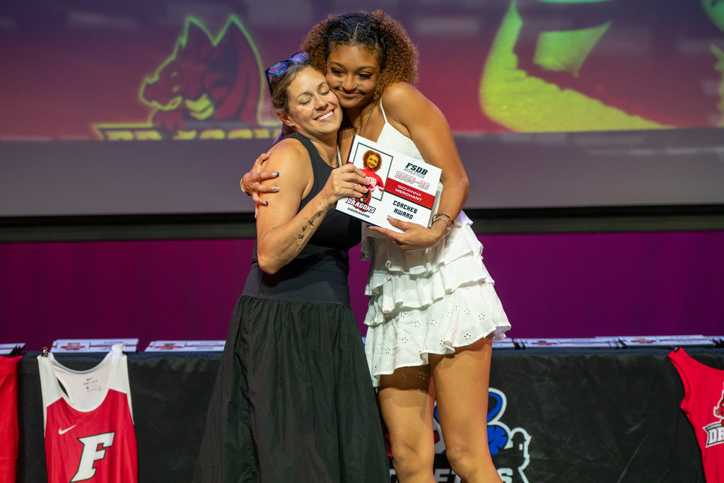 Cheer coach hugs a cheerleader as she accepts her award on stage in Kirk.